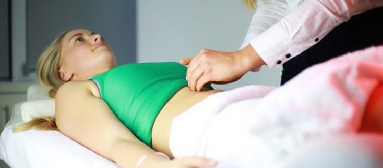 Woman laying on the acupuncture table while practitioner assesses her abdomen.
