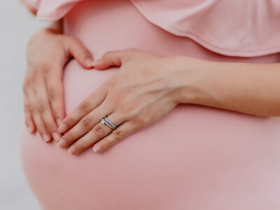 pregnancy woman in pink dress makes a heart with hands over a pregnant belly