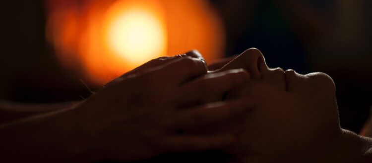 Woman laying in the darkness having a head massage with a light in the distance