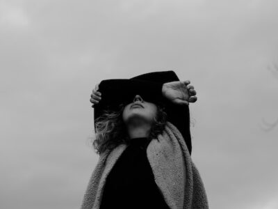 Grayscale photo of woman in a coat with arms covering her face